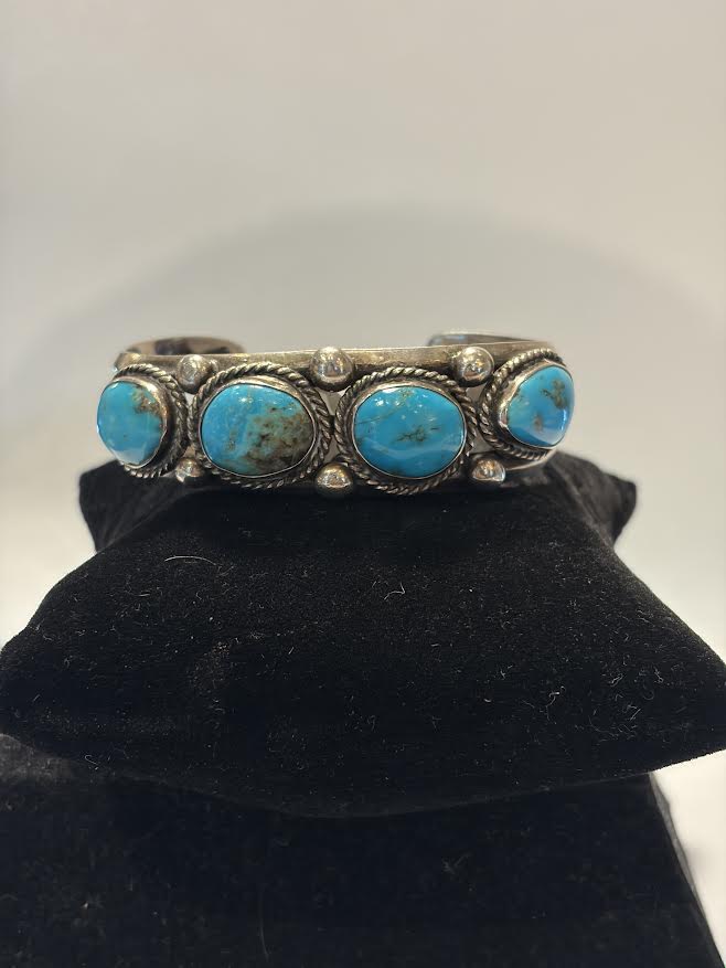 A silver cuff bracelet featuring four round turquoise stones, 