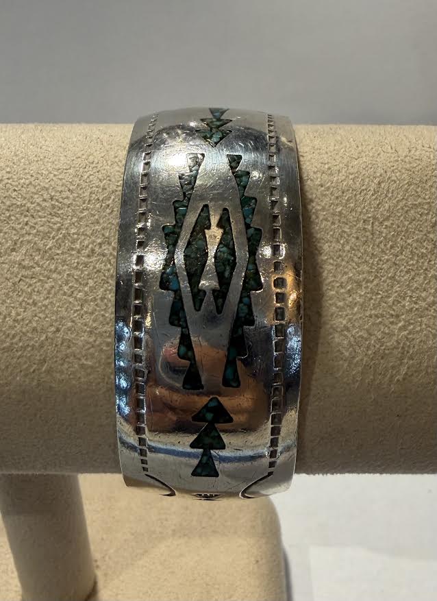 A wide sterling silver cuff bracelet with intricate turquoise inlay patterns