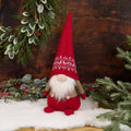 Christmas gnome with red hat and outfit in a snowy scene with greenery