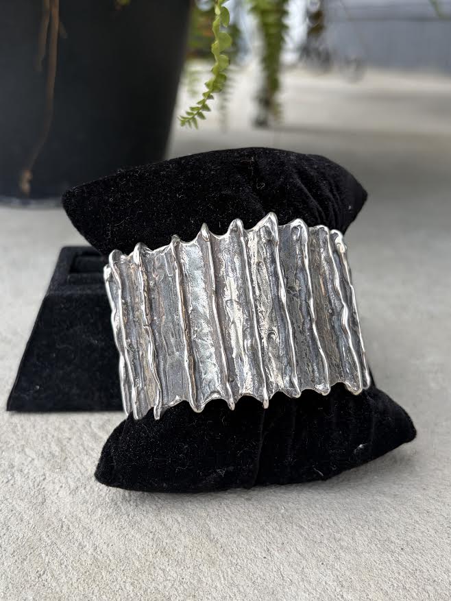A wide silver cuff bracelet with a textured, wavy vertical design, 