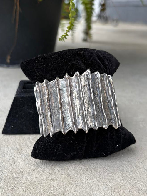 A wide silver cuff bracelet with a textured, wavy vertical design, 
