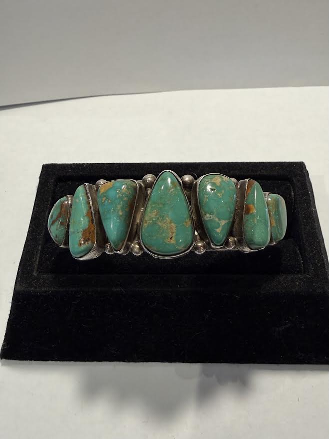 A silver cuff bracelet featuring seven polished turquoise-colored stone 