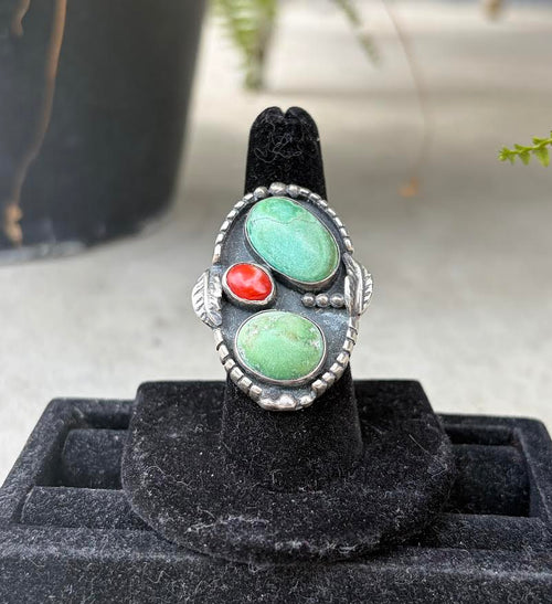 A silver ring with two oval turquoise stones and one small round coral stone