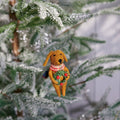 Dog-shaped Christmas ornament with a wreath hanging on a decorated tree.