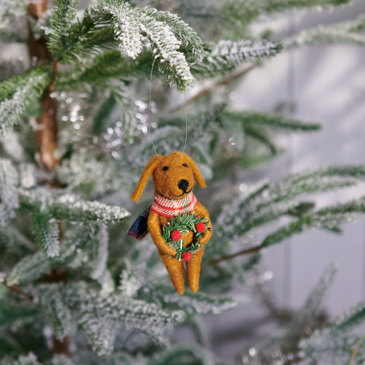 Dog-shaped Christmas ornament with a wreath hanging on a decorated tree.